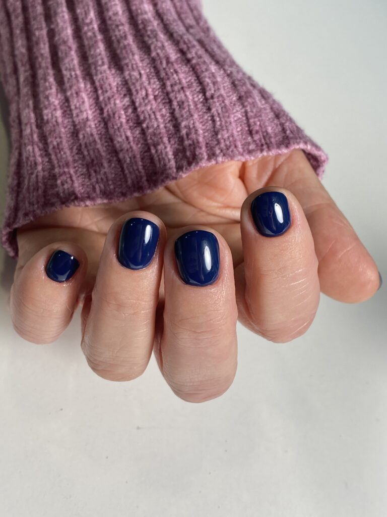 Manicura con esmalte de gel de color azul marino intenso y brillante en uñas cortas y redondeadas, destacando la cobertura y el acabado profesional.