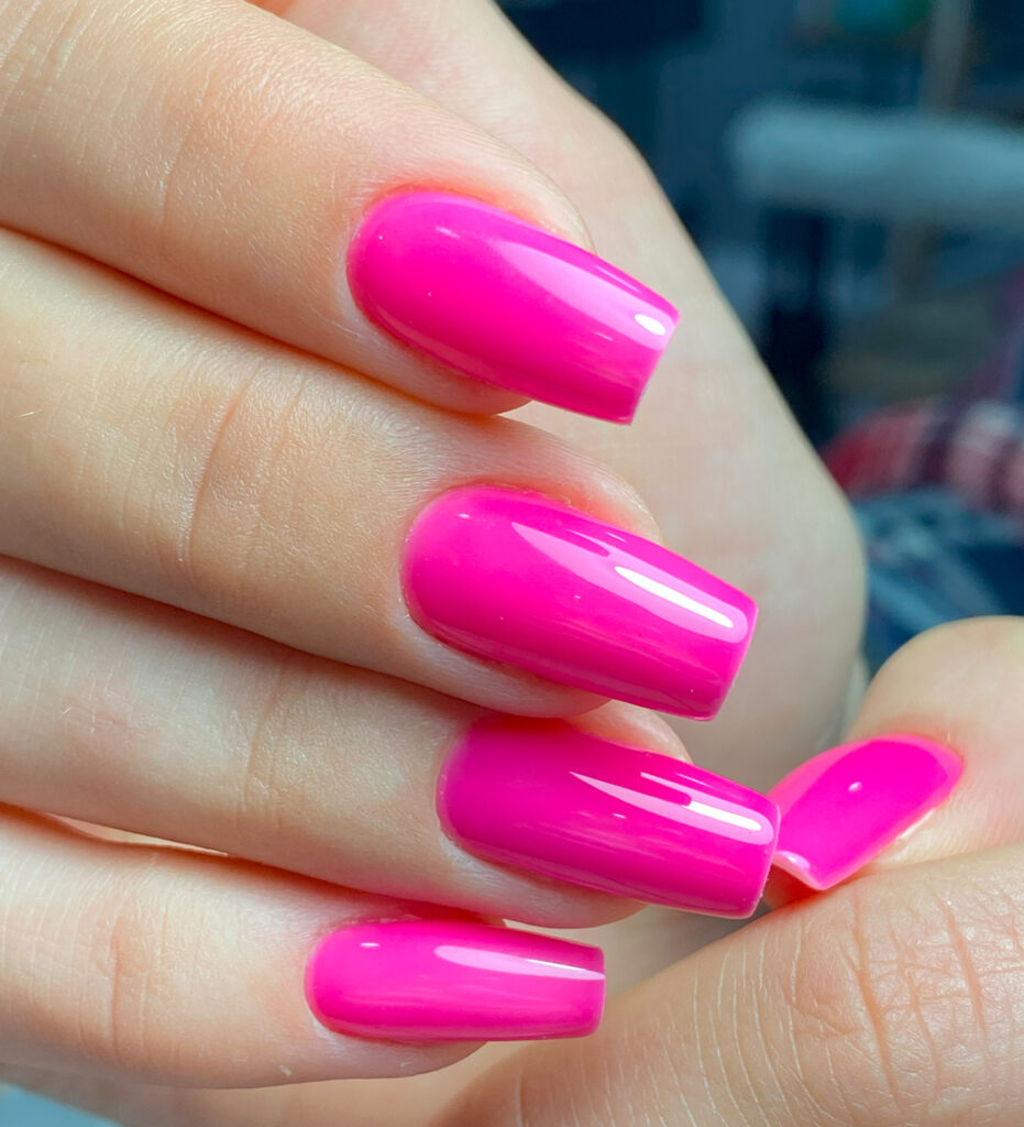 Primer plano de manicura con uñas de longitud media con forma cuadrada, pintadas con un esmalte de gel de color rosa fucsia vibrante y brillante.