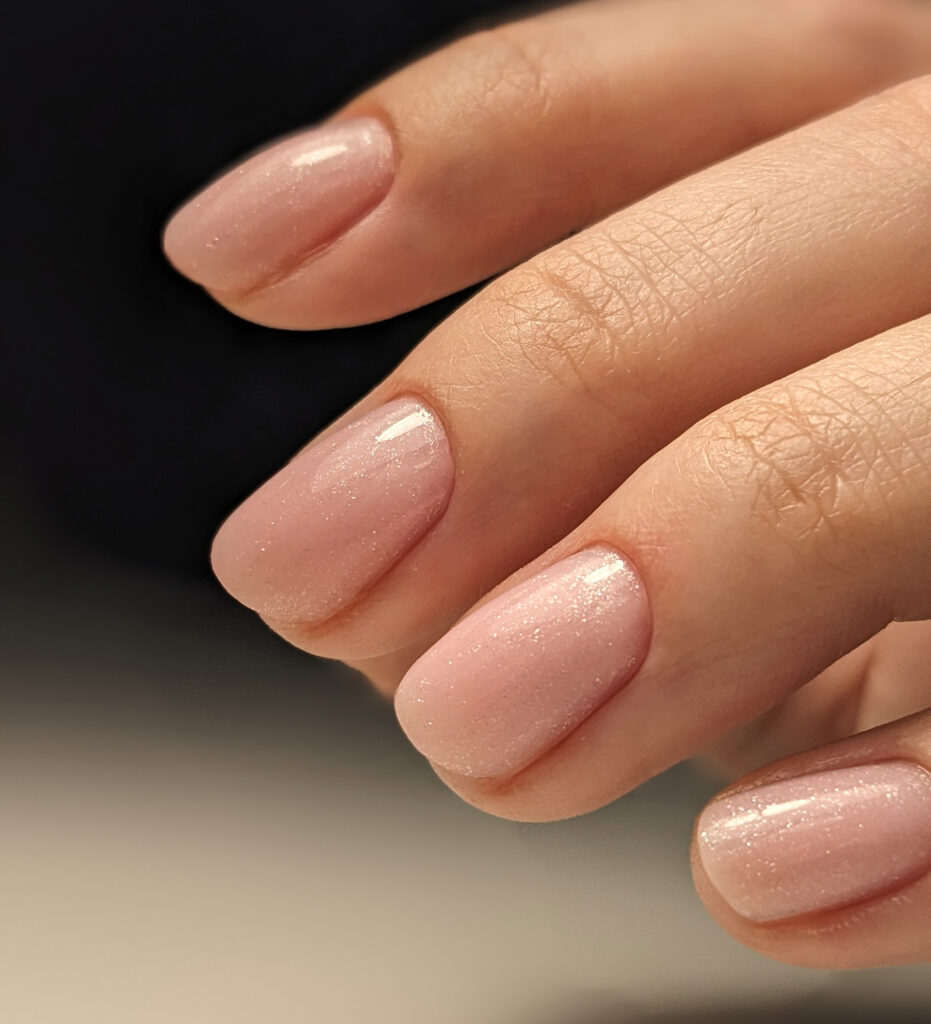 Primer plano de una manicura de uñas cortas con acabado en gel de color rosa claro natural o nude, con un sutil brillo o glitter.