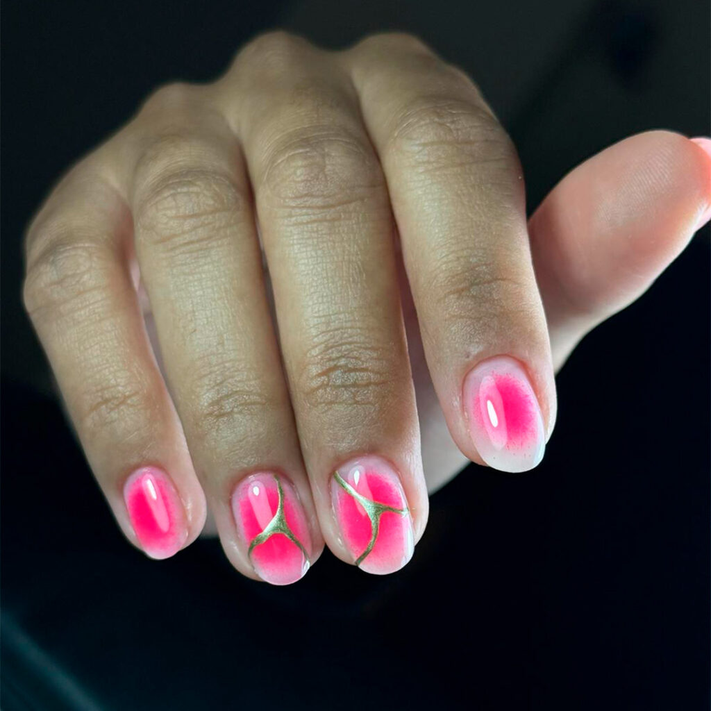 Manicura artística con esmalte de gel rosa neón brillante, decorada con un diseño de líneas doradas finas que simulan el estilo Kintsugi.